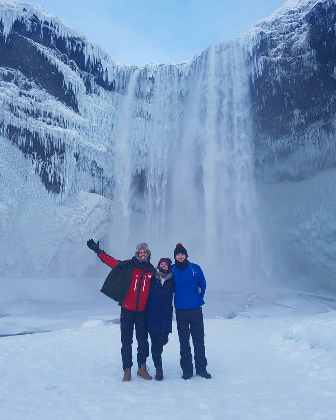 A photograph of Manuel and two of his friends in Iceland. 
                    To their back they have Skógafoss waterfall.