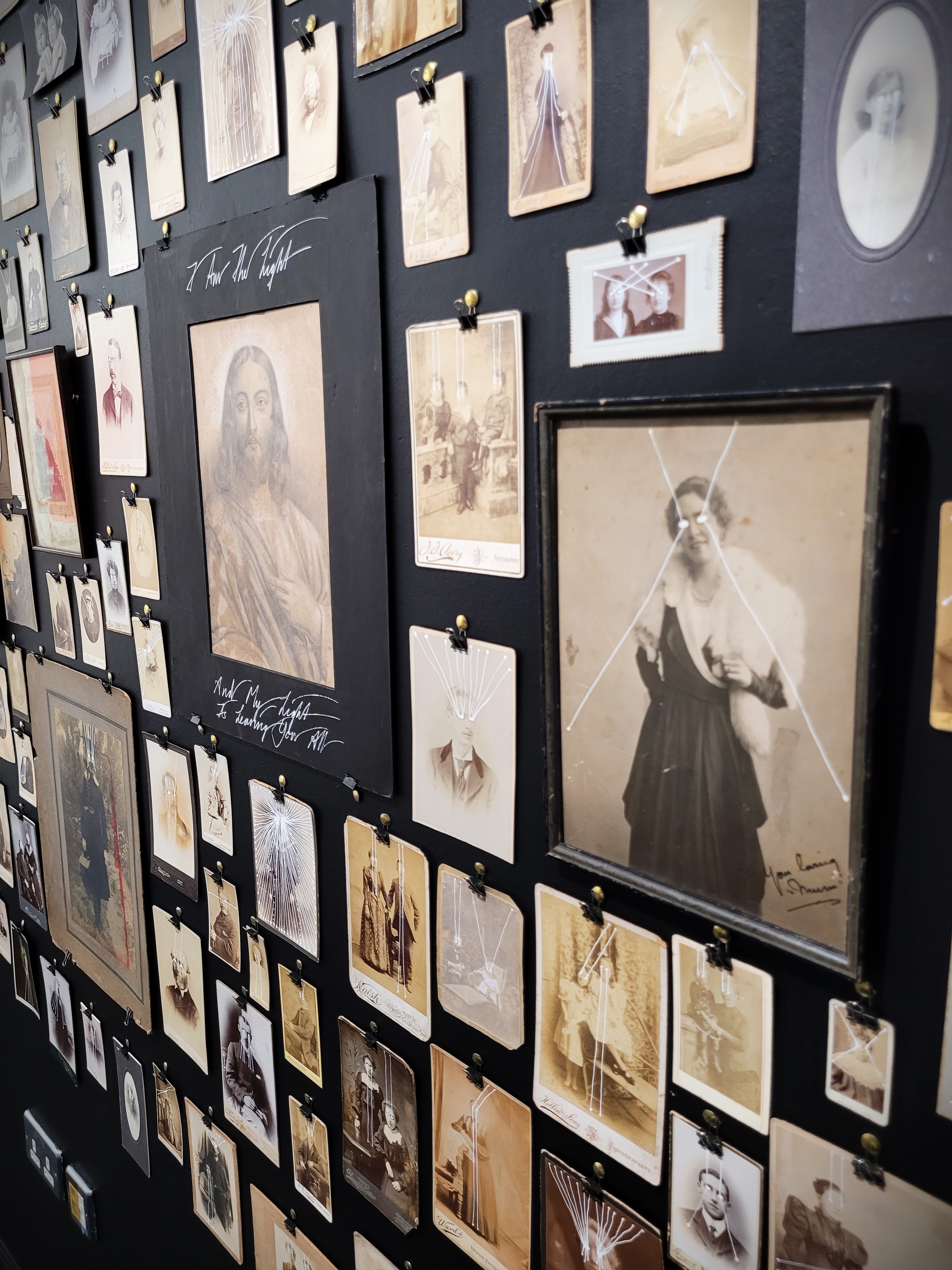 Another photograph of the exhibition; old portraits piled up in a wall with white 
                            beams ejecting from their eyes.